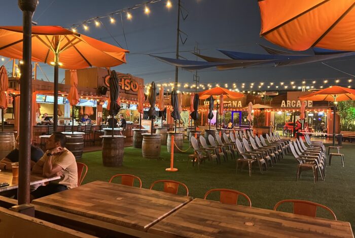 OHSO Brewery Gilbert patio at night with the OHSO sign, barrel tables, lounge chairs and string lights