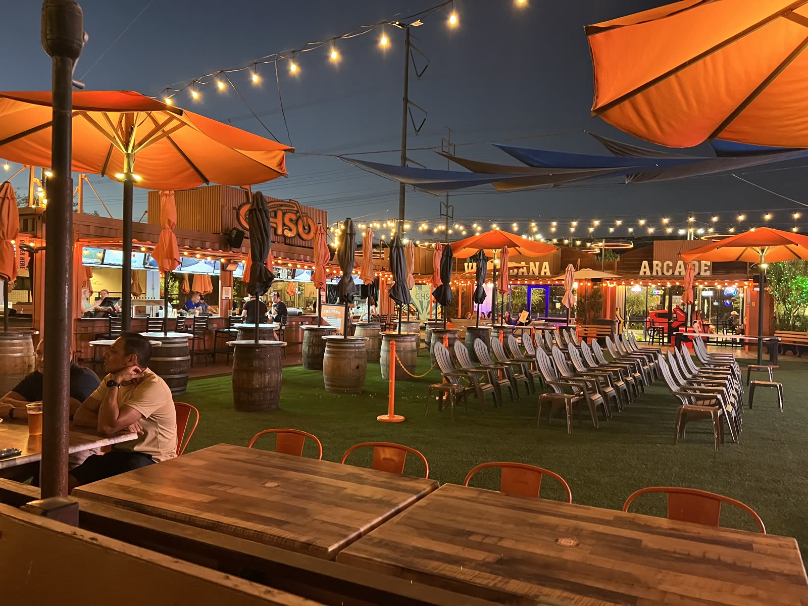OHSO Brewery Gilbert patio at night with the OHSO sign, barrel tables, lounge chairs and string lights